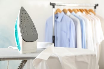 Iron sitting on ironing board next to a rack of clothes